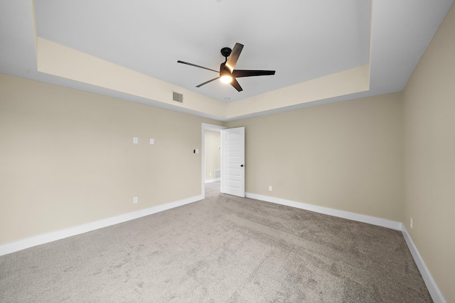 carpeted empty room featuring a ceiling fan, a raised ceiling, visible vents, and baseboards