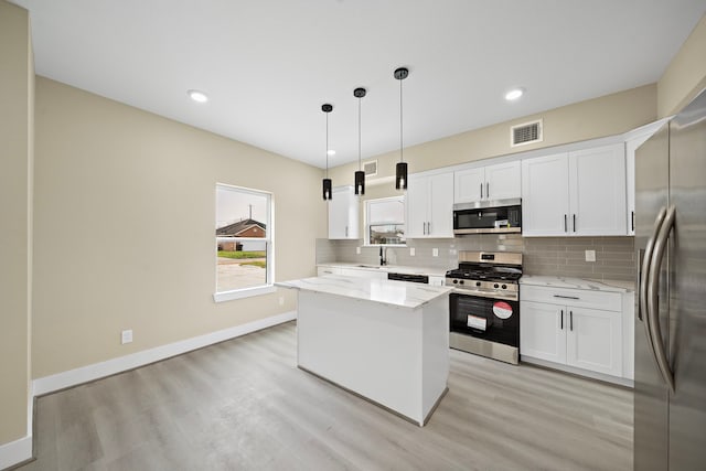 kitchen featuring visible vents, white cabinets, a kitchen island, hanging light fixtures, and stainless steel appliances