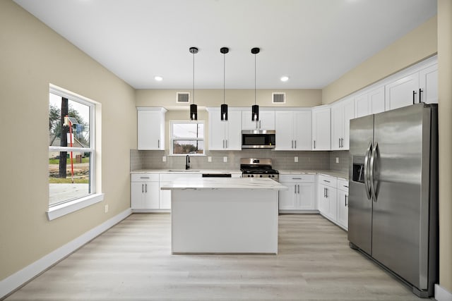 kitchen featuring a center island, decorative light fixtures, stainless steel appliances, white cabinetry, and a sink