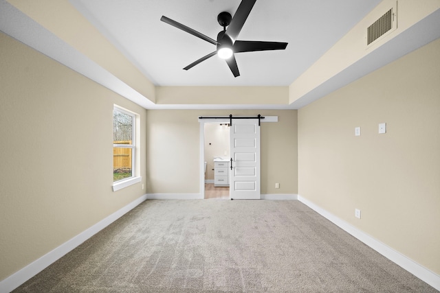 unfurnished bedroom featuring ceiling fan, a barn door, visible vents, baseboards, and carpet