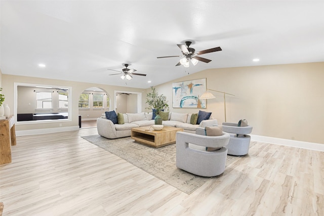 living room with light wood-style floors, baseboards, arched walkways, and vaulted ceiling