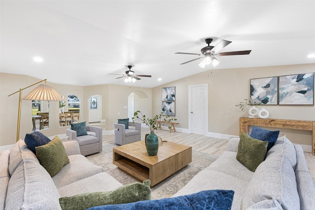 living area with arched walkways, light wood finished floors, vaulted ceiling, ceiling fan, and baseboards