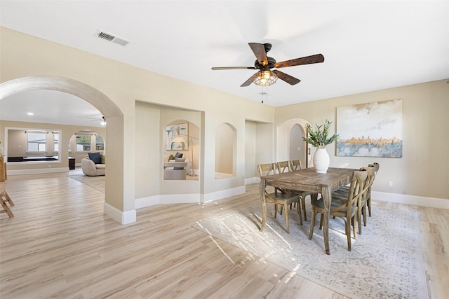 dining room featuring light wood-type flooring, visible vents, arched walkways, and baseboards