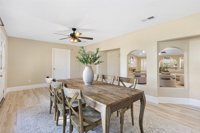 dining room featuring light wood-type flooring, baseboards, visible vents, and arched walkways