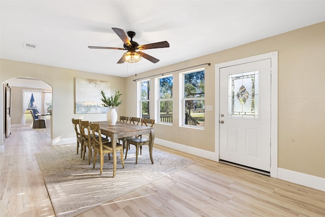 dining space with light wood-type flooring, arched walkways, visible vents, and baseboards