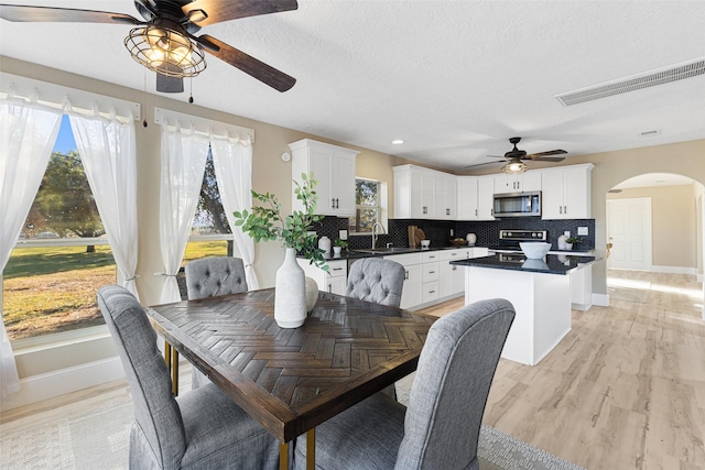 dining space featuring arched walkways, visible vents, light wood-style flooring, a textured ceiling, and baseboards