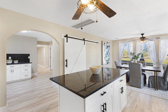 kitchen with light wood finished floors, ceiling fan, a kitchen island, white cabinetry, and backsplash