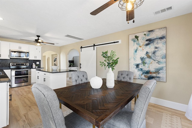 dining space featuring arched walkways, visible vents, ceiling fan, and a barn door