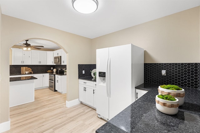 kitchen featuring arched walkways, stainless steel appliances, light wood-style flooring, and white cabinetry