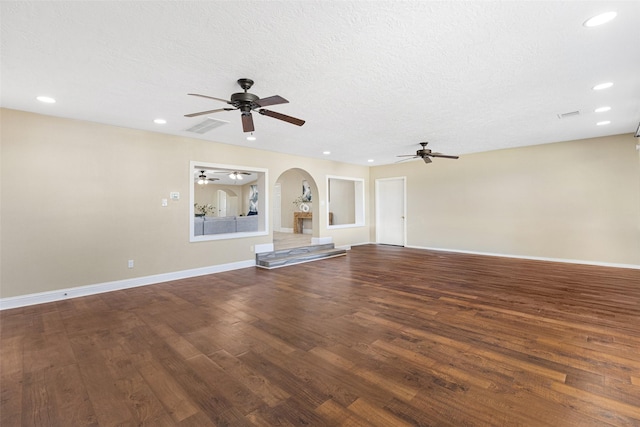 unfurnished living room featuring visible vents, arched walkways, dark wood finished floors, and a textured ceiling