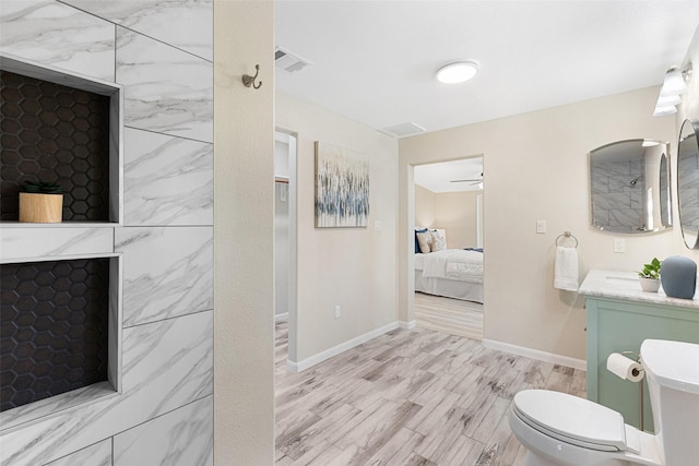 ensuite bathroom featuring toilet, vanity, ensuite bath, wood finished floors, and baseboards