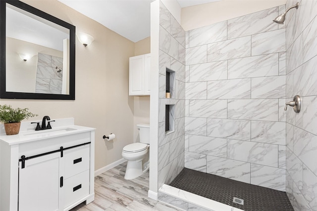 full bathroom featuring baseboards, a tile shower, vanity, and toilet