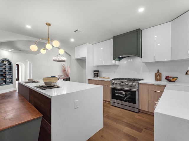 kitchen featuring light countertops, high end stove, white cabinetry, and decorative light fixtures