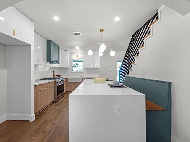 kitchen with white cabinetry, light countertops, appliances with stainless steel finishes, wall chimney range hood, and decorative light fixtures