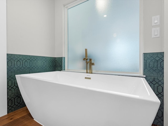 bathroom with tile walls, wood finished floors, a freestanding bath, and wainscoting