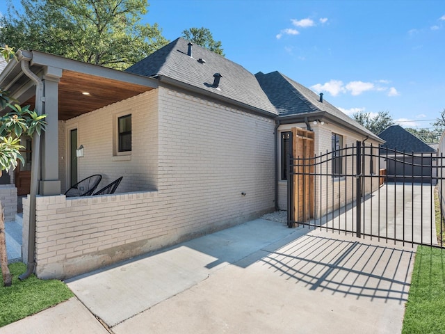 view of property exterior with brick siding, a shingled roof, fence, and a gate