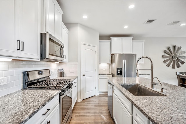 kitchen featuring light stone counters, stainless steel appliances, a sink, visible vents, and white cabinets