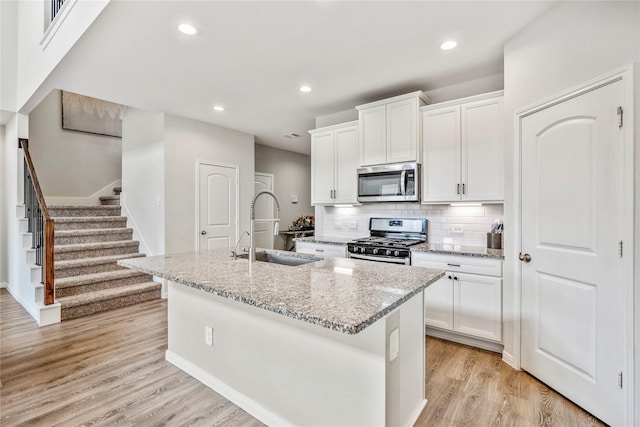 kitchen with stainless steel appliances, white cabinetry, a sink, and an island with sink