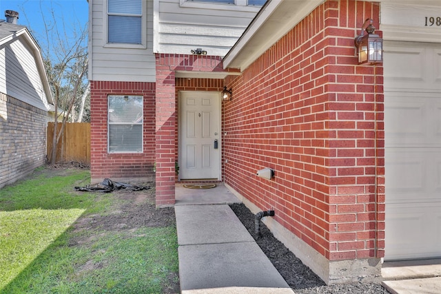 view of exterior entry featuring brick siding, fence, and an attached garage