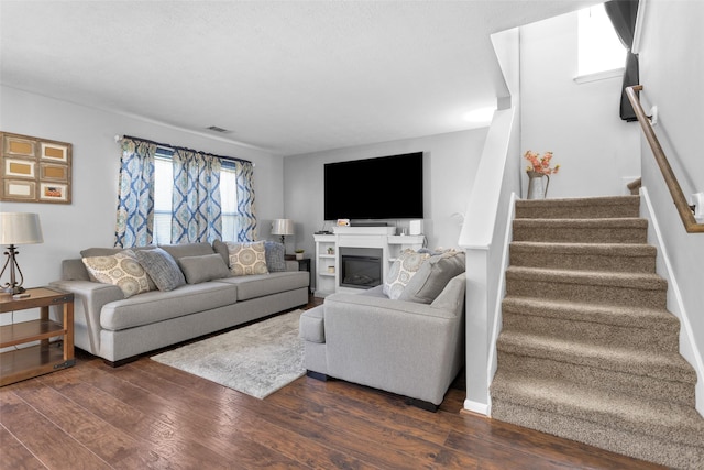 living area with dark wood-type flooring, visible vents, baseboards, stairs, and a glass covered fireplace