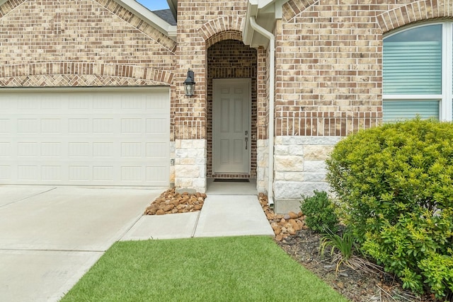 view of exterior entry with a garage, concrete driveway, and brick siding