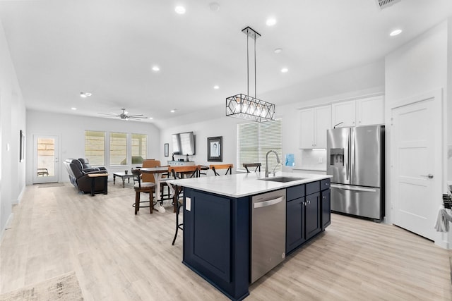 kitchen featuring an island with sink, open floor plan, stainless steel appliances, white cabinetry, and a sink