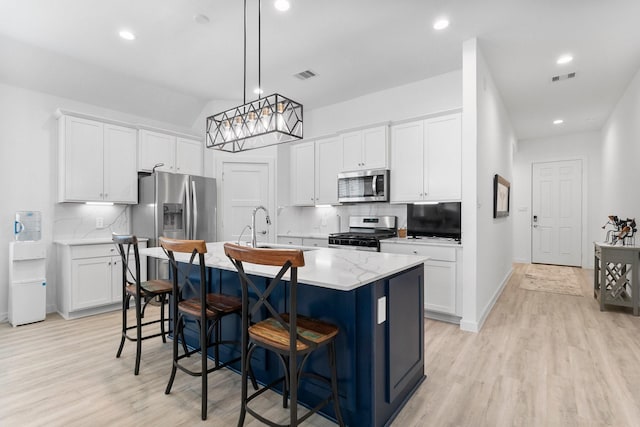 kitchen featuring an island with sink, a breakfast bar area, appliances with stainless steel finishes, hanging light fixtures, and white cabinetry