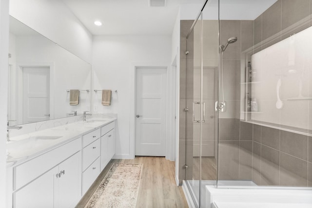 bathroom featuring double vanity, a shower stall, a sink, and wood finished floors