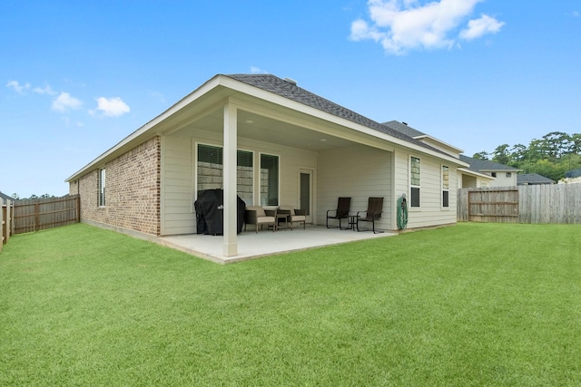 back of house with a fenced backyard, a lawn, brick siding, and a patio