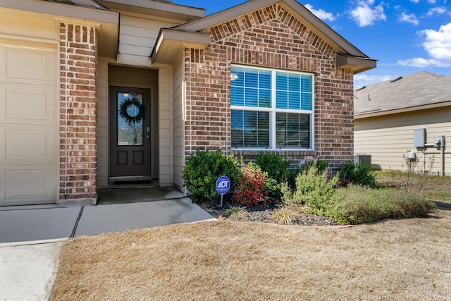 view of exterior entry featuring an attached garage, cooling unit, and brick siding