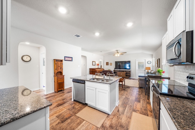 kitchen featuring arched walkways, white cabinets, open floor plan, appliances with stainless steel finishes, and an island with sink