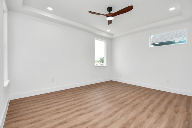 spare room featuring a tray ceiling, recessed lighting, light wood-style flooring, and baseboards