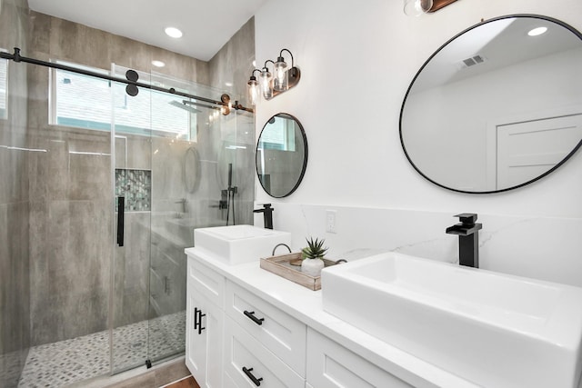 full bath with double vanity, a shower stall, visible vents, and a sink