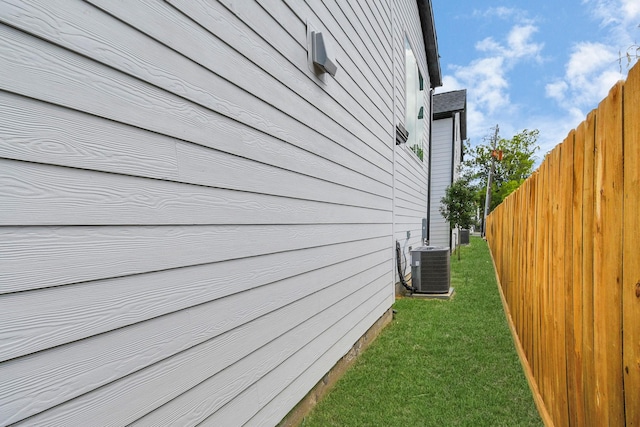 view of side of property featuring a lawn, fence, and central air condition unit