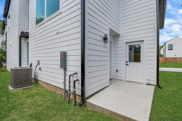 property entrance featuring a lawn, fence, and central air condition unit