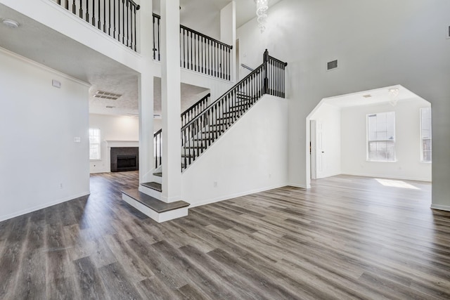 unfurnished living room with a fireplace, stairway, a high ceiling, wood finished floors, and baseboards