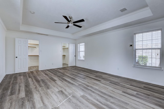 unfurnished bedroom featuring ornamental molding, a tray ceiling, wood finished floors, and visible vents