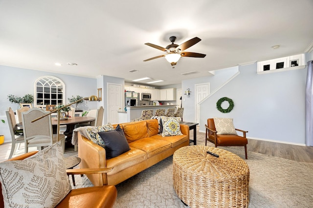 living room with light wood finished floors, a ceiling fan, baseboards, and crown molding