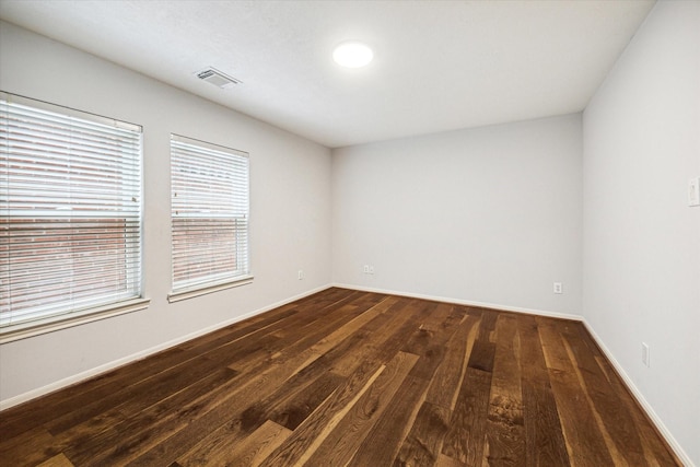 spare room with dark wood-type flooring, visible vents, and baseboards