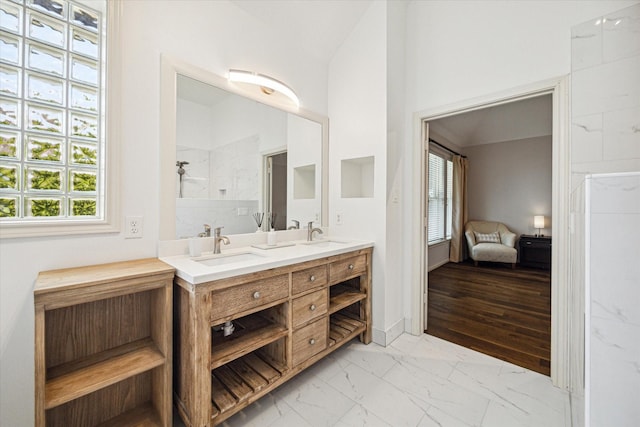 ensuite bathroom with double vanity, marble finish floor, a healthy amount of sunlight, and a sink