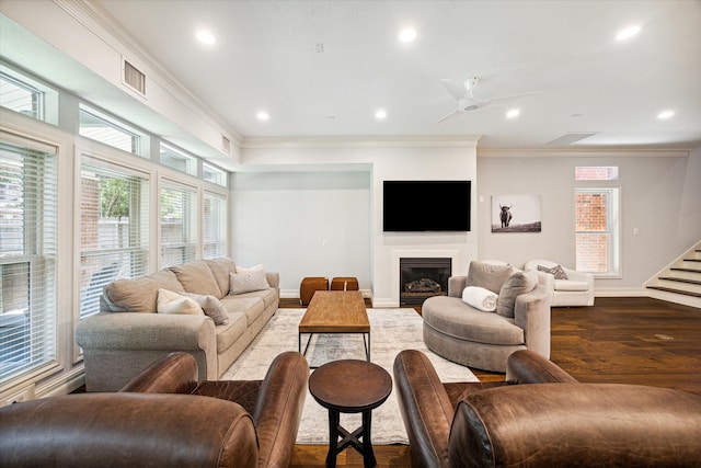 living room with baseboards, visible vents, a glass covered fireplace, ornamental molding, and wood finished floors