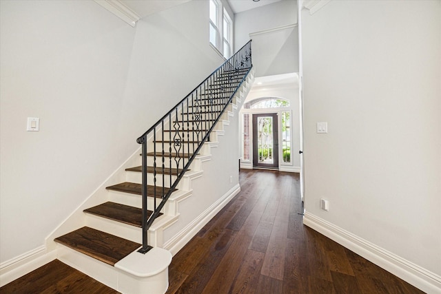 entryway with dark wood-style flooring, a towering ceiling, baseboards, and stairs