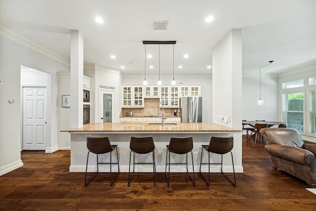 kitchen featuring a breakfast bar area, a sink, hanging light fixtures, freestanding refrigerator, and glass insert cabinets