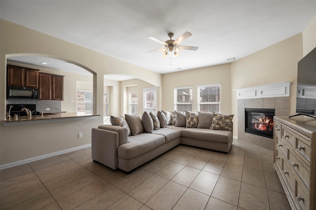 living room with light tile patterned flooring, a fireplace, a ceiling fan, visible vents, and baseboards