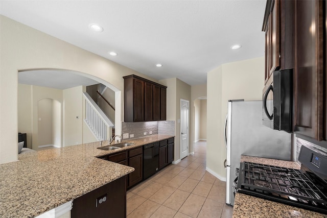 kitchen featuring light stone counters, tasteful backsplash, gas stove, a sink, and dark brown cabinets