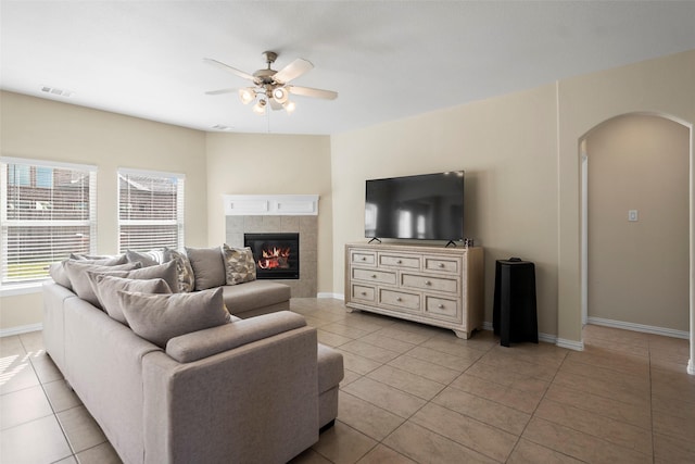 living area with arched walkways, light tile patterned floors, visible vents, a ceiling fan, and baseboards