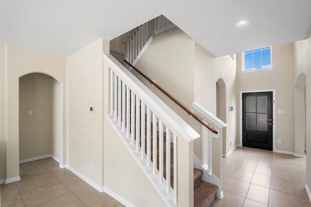 entryway featuring light tile patterned floors, baseboards, stairway, and arched walkways