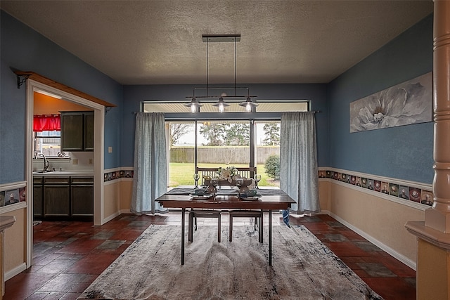 dining room with a textured ceiling, ornate columns, stone tile flooring, and baseboards