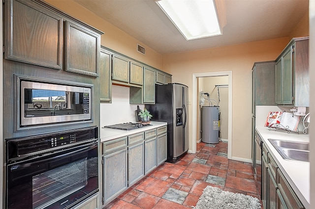 kitchen featuring stone tile floors, light countertops, appliances with stainless steel finishes, electric water heater, and a sink