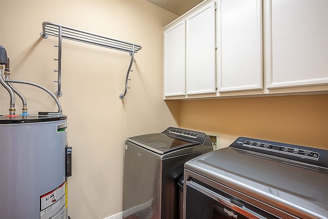 clothes washing area featuring water heater, washing machine and clothes dryer, and cabinet space